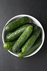 Fresh cucumbers in bowl on dark textured table, top view