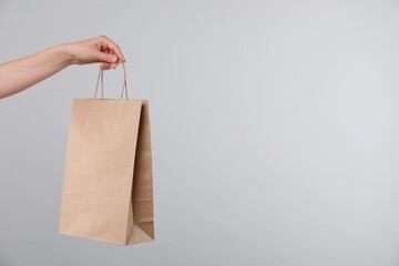 Woman with kraft paper bag on grey background, closeup. Space for text