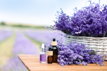 Beautiful lavender flowers and bottles of essential oils on wooden table in field, space for text