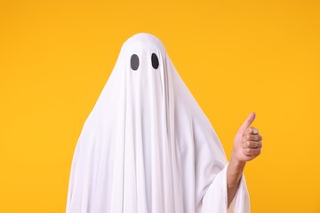 Man in ghost costume showing thumbs up on orange background
