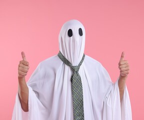 Man in ghost costume with tie showing thumbs up on pink background
