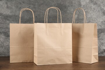 Kraft paper bags on wooden table against grey textured background, closeup