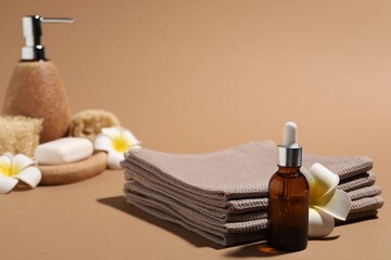 Folded waffle towels, bottle of cosmetic product and plumeria flower on light brown background,...