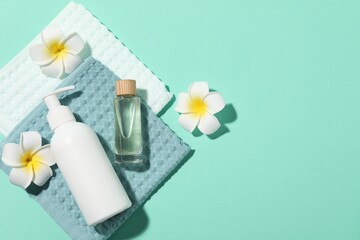 Folded waffle towels, plumeria flowers and spa products on turquoise background, flat lay. Space...