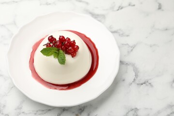 Delicious panna cotta with red currants, sauce and mint on white marble table
