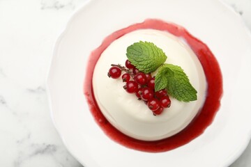 Delicious panna cotta with red currants, sauce and mint on white marble table, top view