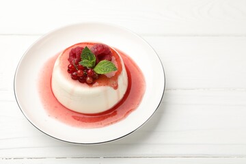 Delicious panna cotta with berries, sauce and mint on white wooden table, closeup