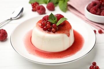 Delicious panna cotta with berries, sauce and mint on white wooden table, closeup