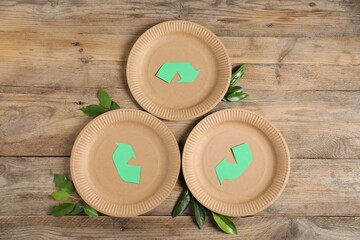 Eco friendly packaging. Recycling symbol, paper plates and leaves on wooden background, flat lay