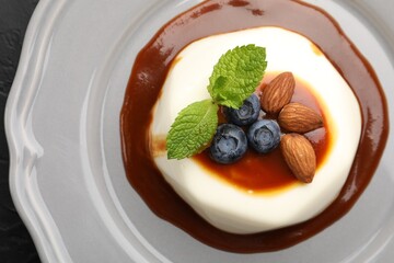 Tasty panna cotta with blueberries, almonds and sauce on black table, top view