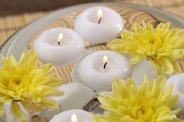 Burning candles and flowers in bowl of water on table, closeup