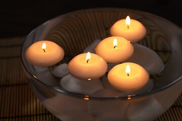 Burning candles in bowl of water on bamboo mat, closeup
