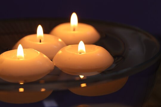 Burning candles in bowl of water on dark purple background, closeup - Powered by Adobe