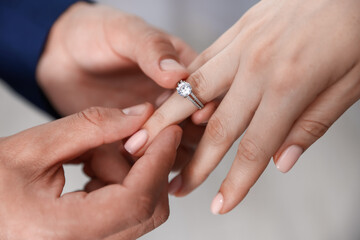 Making proposal. Man putting engagement ring on his girlfriend's finger indoors, closeup