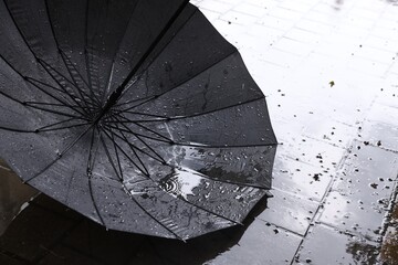 Black umbrella on wet asphalt under heavy rain, closeup. Space for text