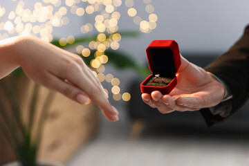 Man with engagement ring making marriage proposal to his girlfriend indoors, closeup. Bokeh effect