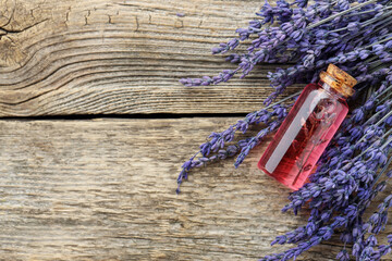 Lavender essential oil in bottle and flowers on wooden table, top view. Space for text