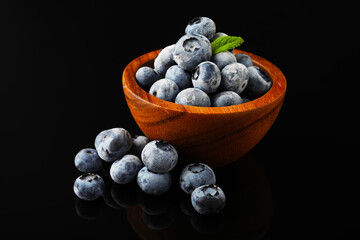 Many frozen blueberries in bowl on black table, closeup