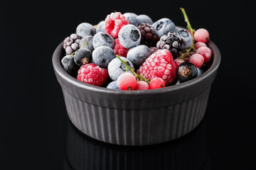 Many different frozen berries in bowl on black table, closeup