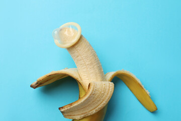Sex education. Banana with condom on light blue background, top view