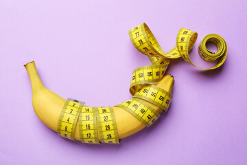 Sex education. Banana with measuring tape on violet background, top view