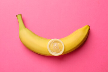 Sex education. Banana with condom on pink background, top view
