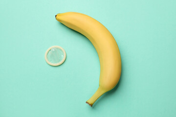 Sex education. Banana and condom on turquoise background, flat lay