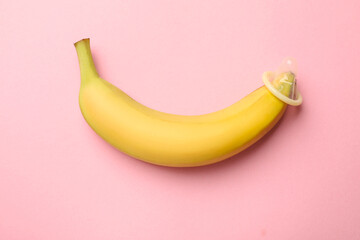 Sex education. Banana with condom on pink background, top view