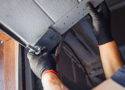 Close-up of a worker attaching rollers to the metal tracks of a garage door during installation or repair.