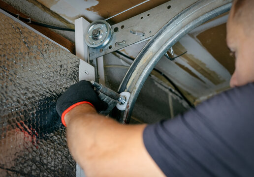 Close-up of a worker attaching rollers to the metal tracks of a garage door during installation or repair.