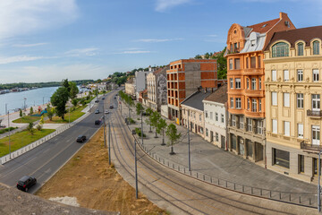 Sunny urban waterfront in Belgrade: Sava River, wide promenade with tram tracks, historic buildings under blue sky. Perfect for city life and travel themes