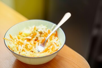 Fresh vegan coleslaw salad with white cabbage and carrots in a yellow ceramic bowl, healthy plant-based meal on table