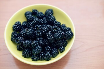 Ripe dark purple blackberries in a yellow ceramic bowl on a wooden table, fresh and healthy summer fruits