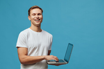 smiling man holding laptop standing over blue background working digital nomad freelance technology...