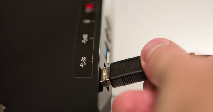 White masculine looking hand connects and disconnects a USB cable to computer connection port.