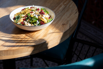 Fresh Green Crunch non-veg salad with kale, grilled mushroom, beans, olives, chicken, feta, cranberry, nuts, and carrot orange vinaigrette on a brown table in warm sunlight.