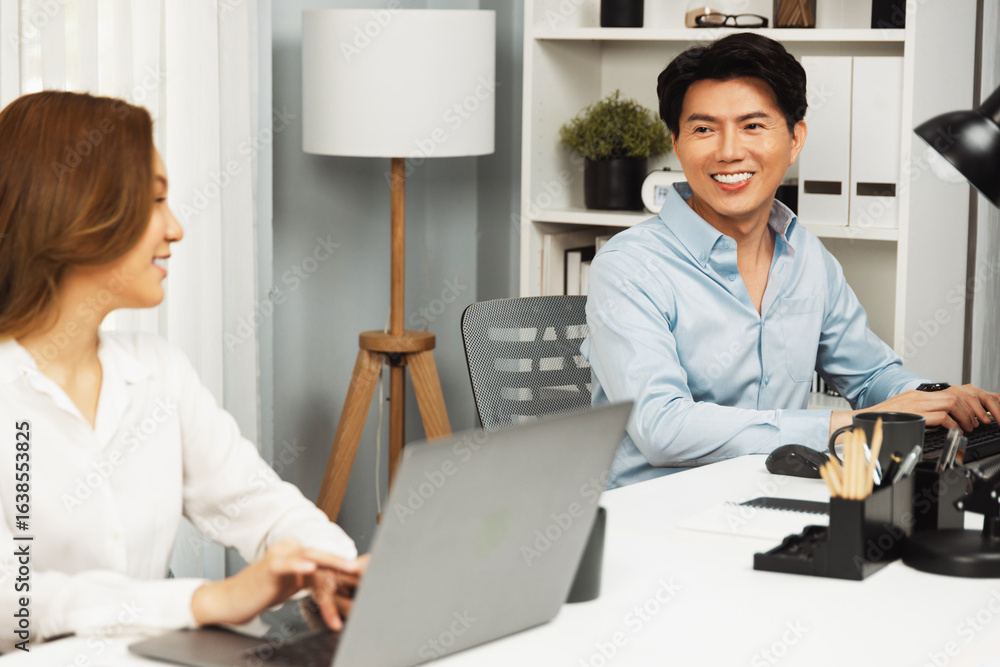 Poster smiling asian man talking with woman colleague in planning marketing report project on laptop casual