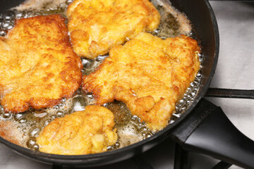 Golden fried chicken fillets sizzling in hot oil on a black frying pan over gas stove. Homemade crispy breaded meat preparation. Traditional cooking process of fried chicken breast cutlets.