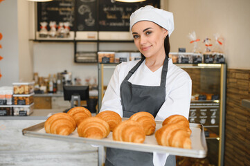 Baker woman holding tray of freshly baked croissants in bakery