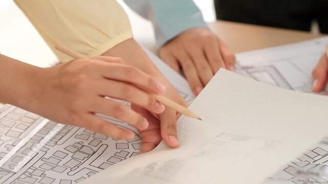 Smart architect and safety engineer discussion about building blueprint on table with architectural document, measurement tools and wooden block scatter around at modern office. Closeup. Delineation.