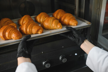 Baker taking tray of freshly baked croissants out of oven