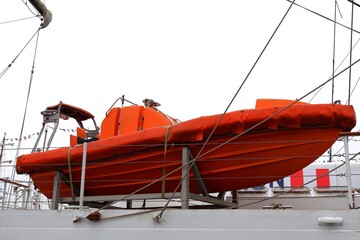 An orange lifeboat hanging on the side of a tall ship