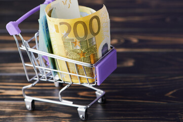 Shopping cart filled with rolled banknotes on wooden table