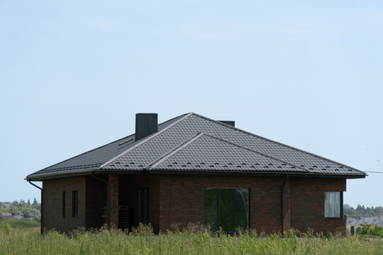 Newly constructed brick house in a rural area surrounded by tall grass on a clear sunny day