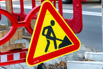 Warning sign indicating construction activity on a busy urban street during daylight hours
