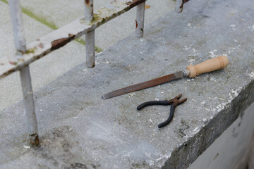 Pliers and a file on a concrete window sill.