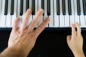 father and son playing the keys of a piano