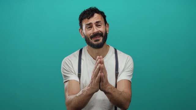 Hispanic man with beard gesturing for begging against a green background, wearing a white shirt and suspenders, expressing emotion through hand movements and facial expressions.