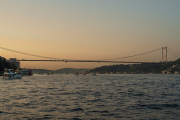 Obraz premium Scenic Bosphorus Strait in Istanbul at sunset with urban skyline, iconic bridges, fishing boats, and calm sea, highlighting the beauty and cultural heritage of Turkey’s most famous waterway
