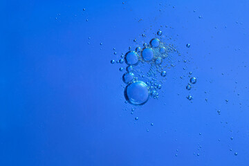 Macro image of a group of oil bubbles floating in water against a solid blue background. Copy space